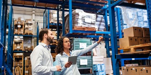 Businesswoman with a digital tablet showing and talking with male worker in distribution warehouse. Manager working with foreman in warehouse checking stock levels.
